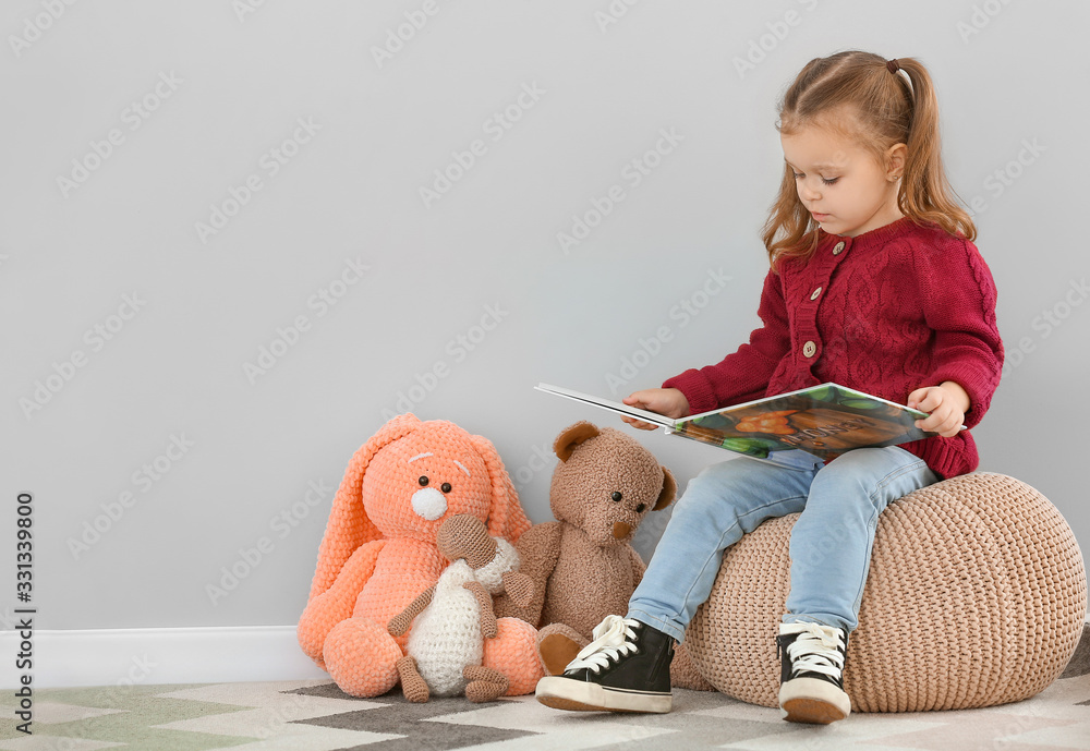 Cute little girl reading book near grey wall