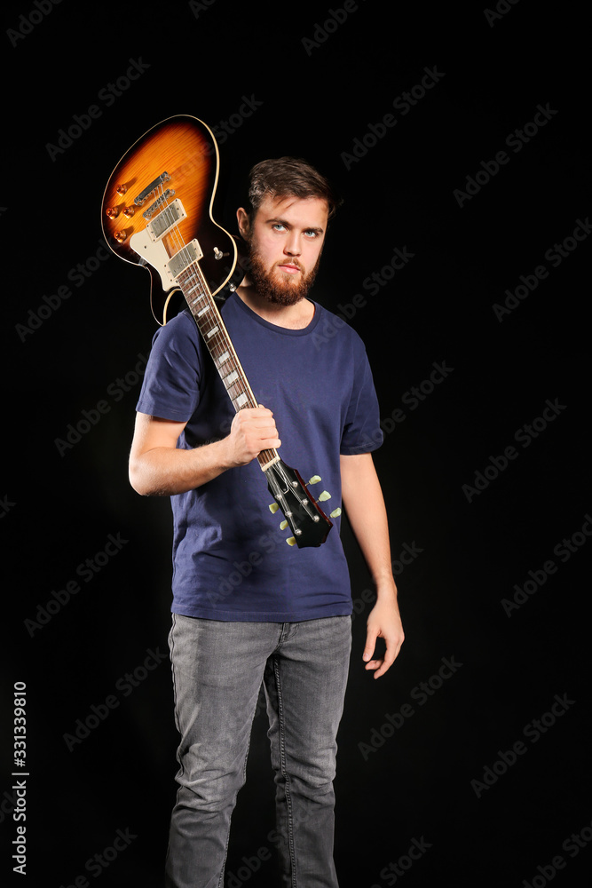 Young man with guitar on dark background