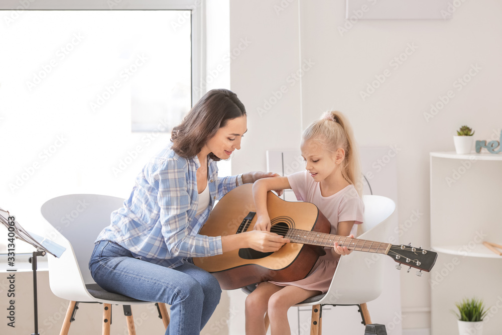 Private music teacher giving guitar lessons to little girl at home