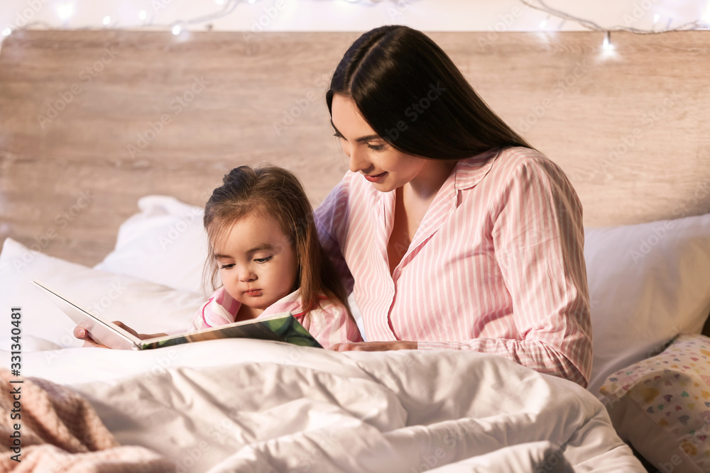 Mother and her little daughter reading bedtime story at home