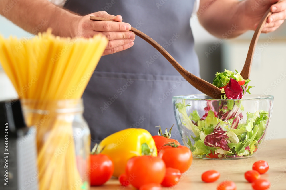 Handsome male chef making salad in kitchen, closeup