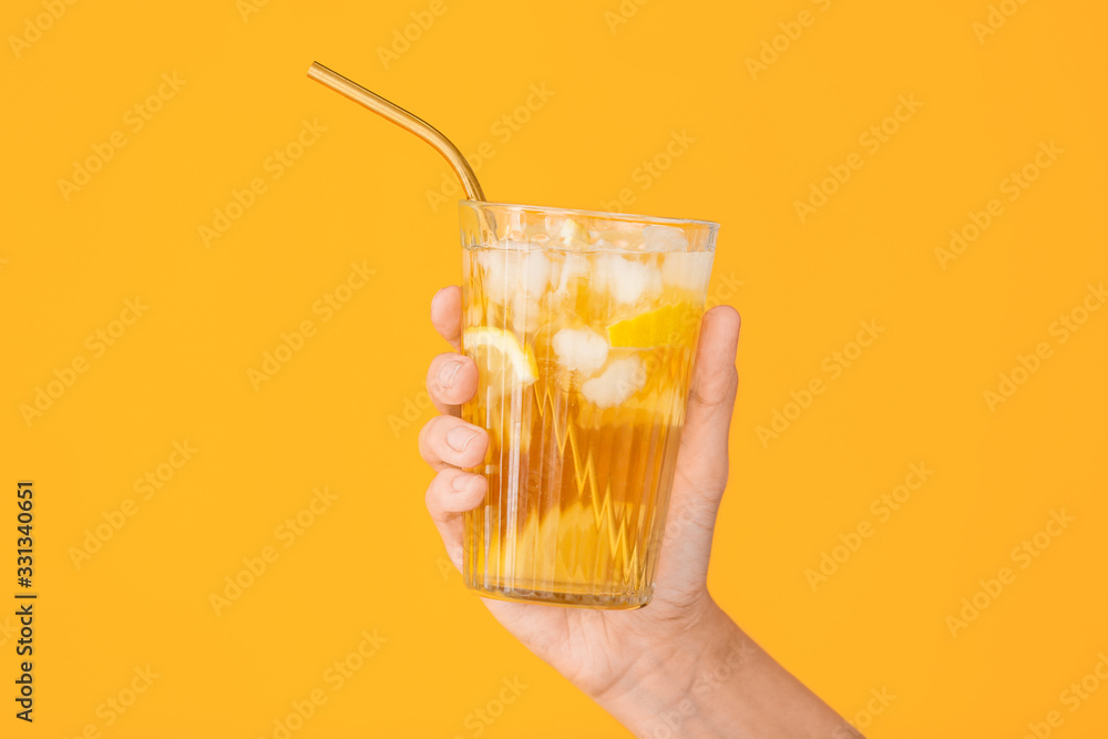 Female hand with cold tea in glass on color background