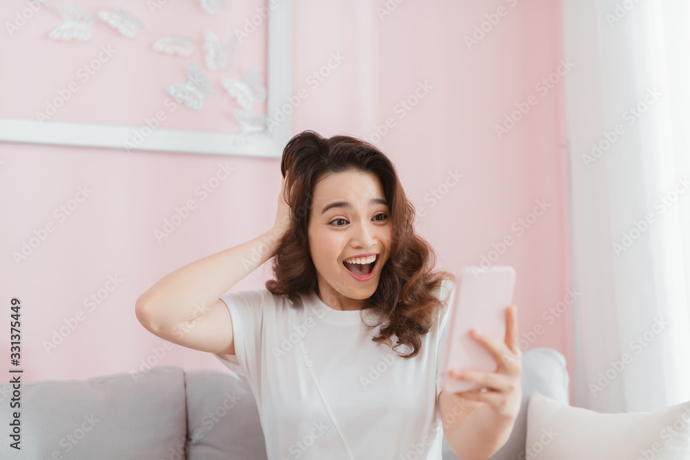 surprised shocked woman looking at phone screen sitting on a sofa in apartment at home