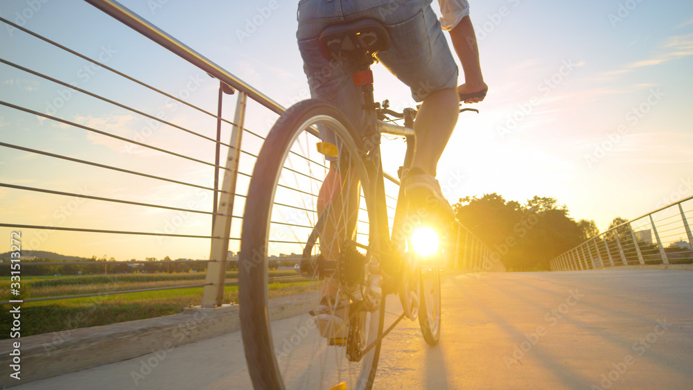 LENS FLARE: Unrecognizable man pedals his bicycle across an overpass at sunrise.