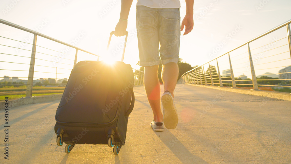 LOW ANGLE Unrecognizable man in shorts walks across an overpass with his luggage