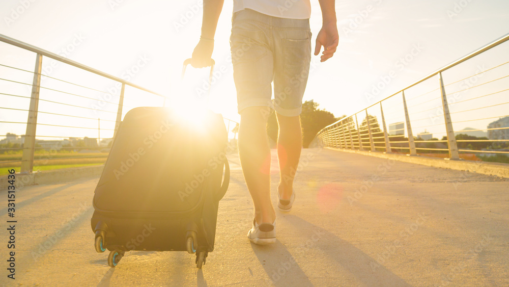 LENS FLARE: Young digital nomad drags his suitcase to the airport at sunrise.