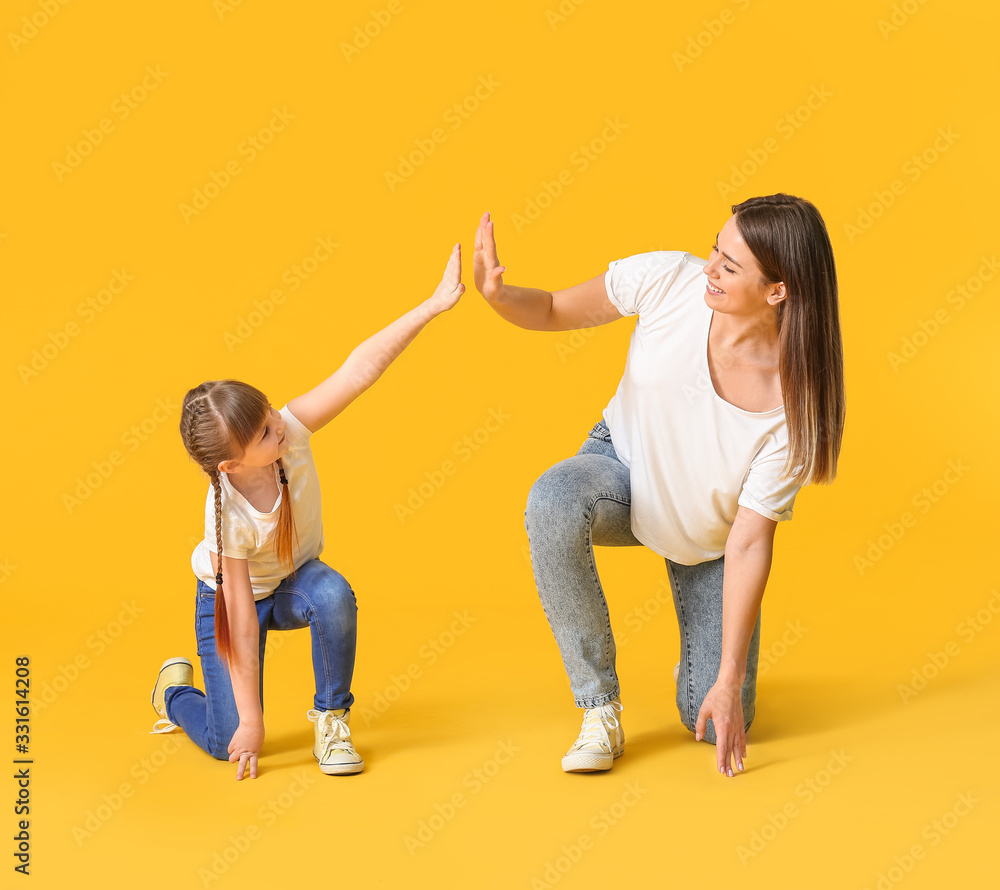 Happy mother and her little daughter dancing against color background