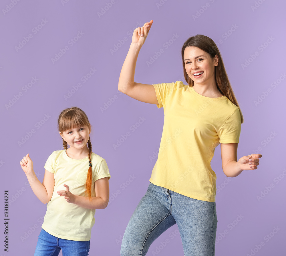 Happy mother and her little daughter dancing against color background