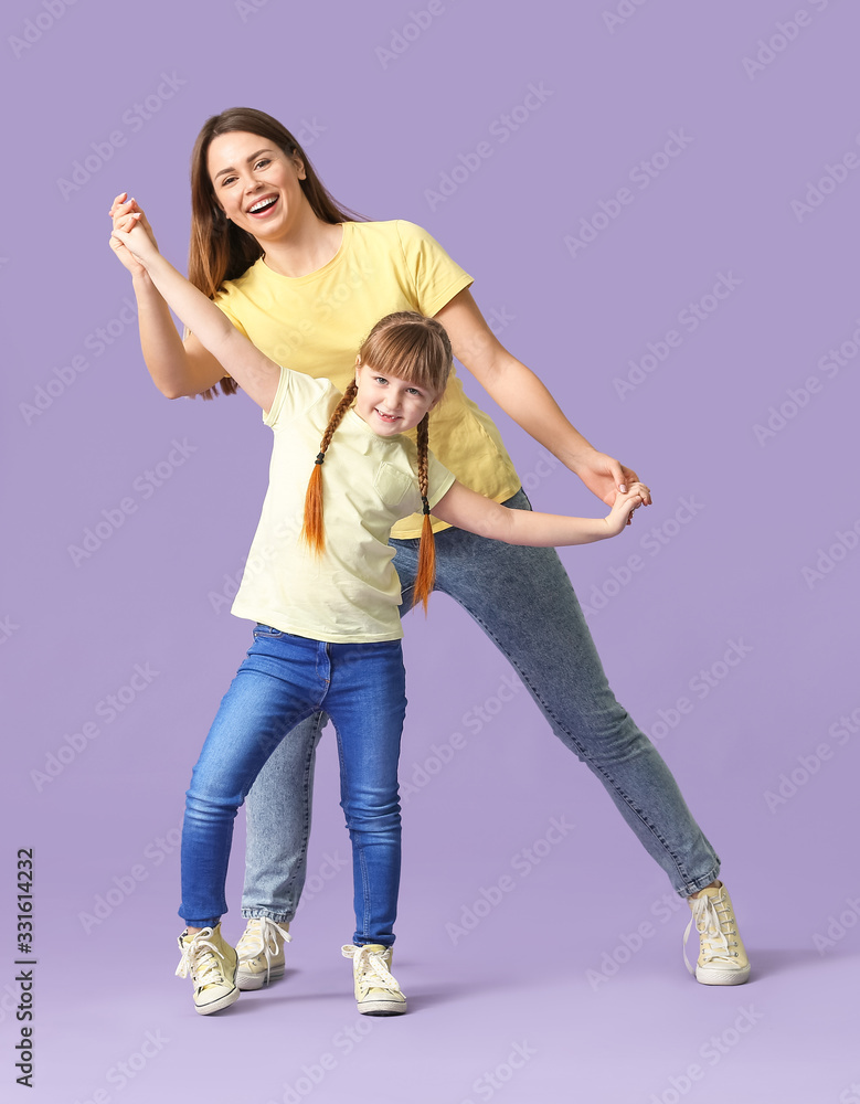 Happy mother and her little daughter dancing against color background