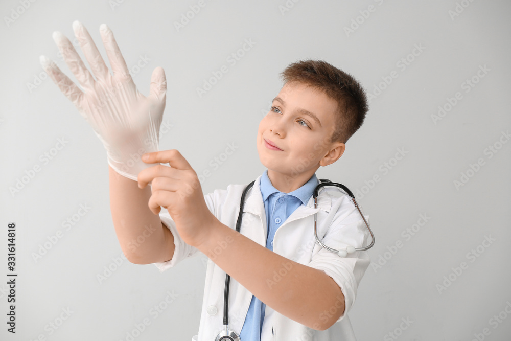 Cute little doctor wearing gloves on grey background