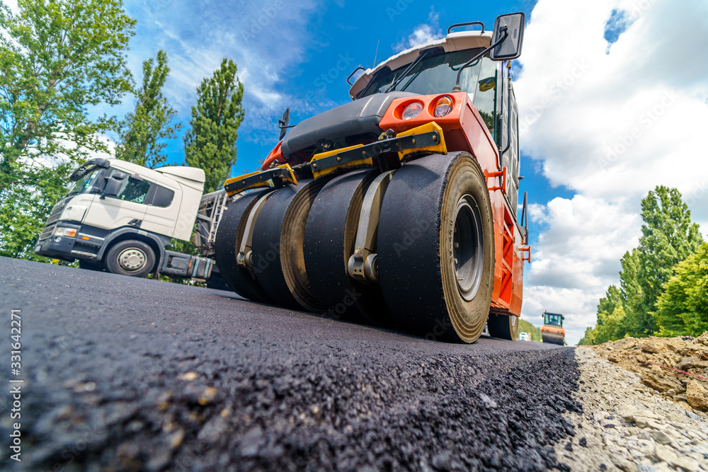 Road repair, compactor lays asphalt. Heavy special machines. Asphalt paver in operation. Side view. 