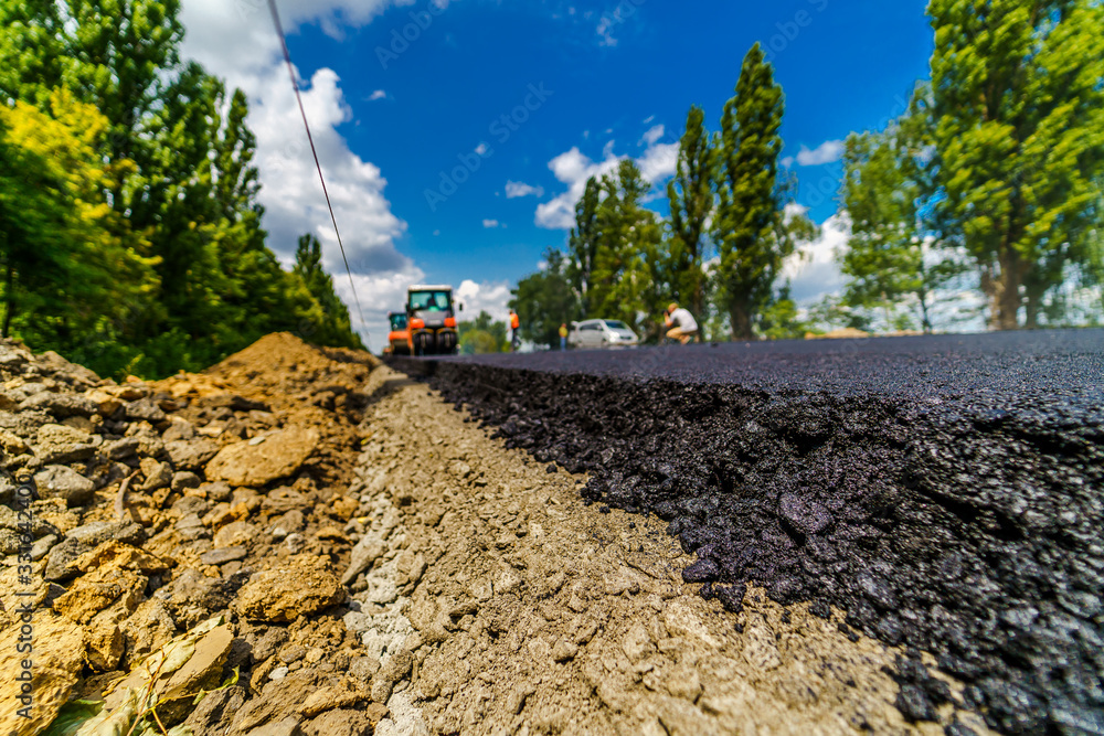 Fresh asphalt on highway construction site. Industrial pavement machine laying.