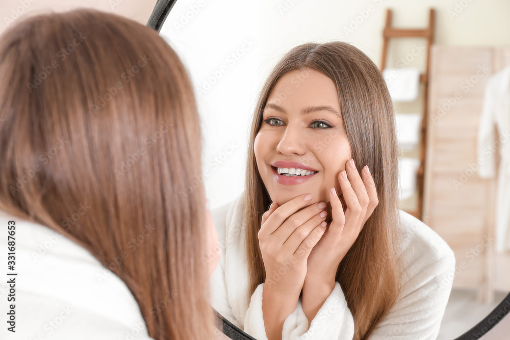 Beautiful young woman with healthy skin looking in mirror