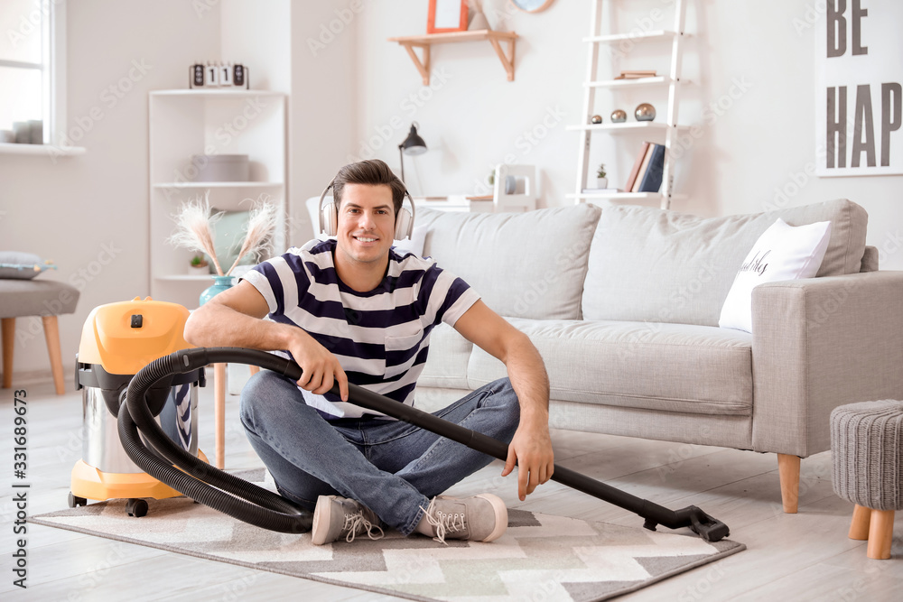 Young man listening to music while hoovering floor at home