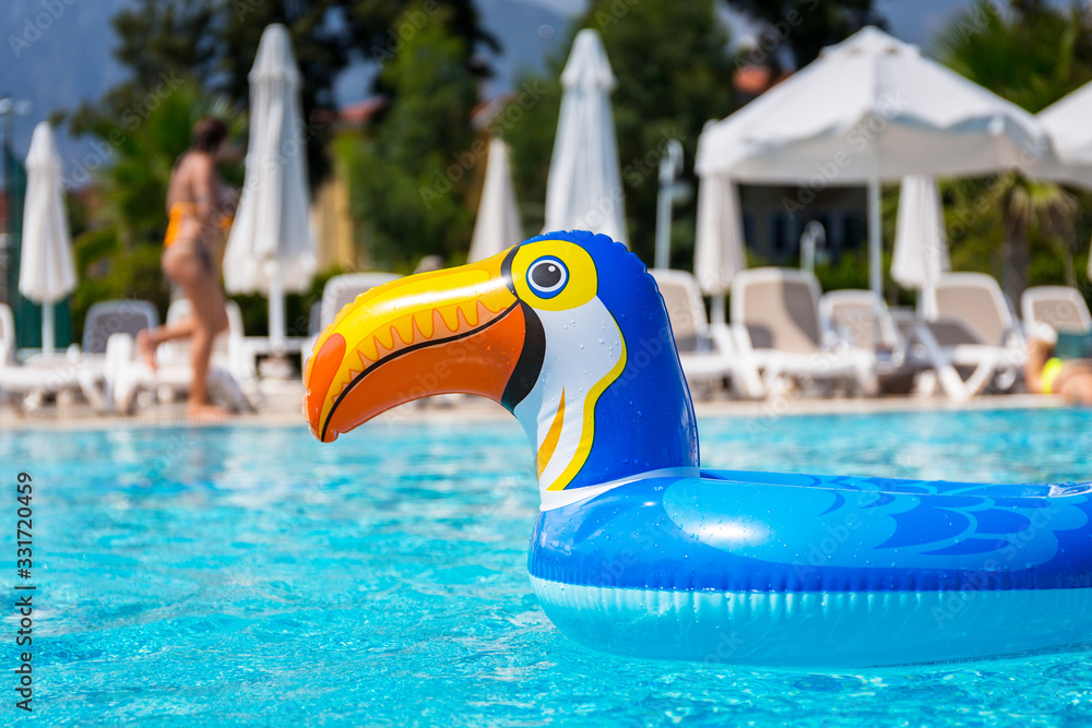 Empty float ring in toucan shape on the blue swimming pool