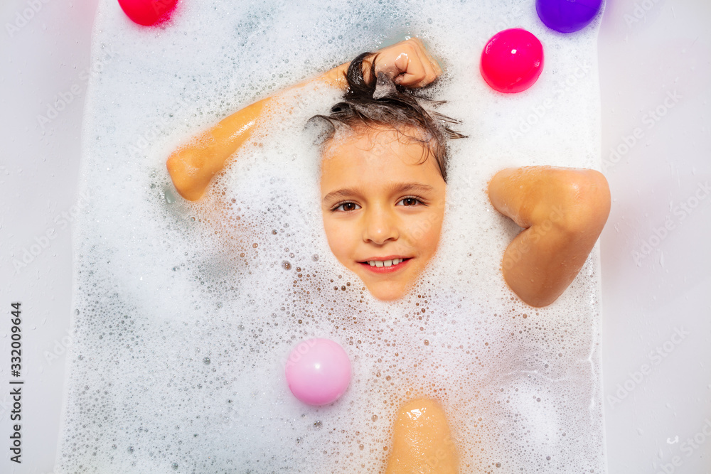 Cute boy with big smile swim on the back in soap at home bath washing hair