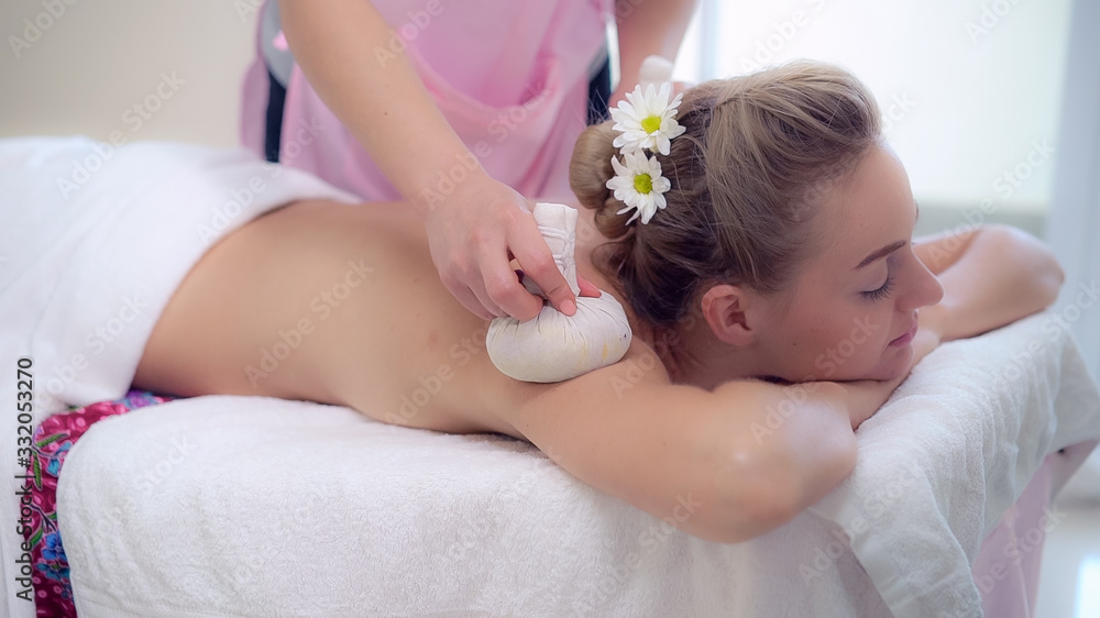 Massage therapist using herbal compress with woman