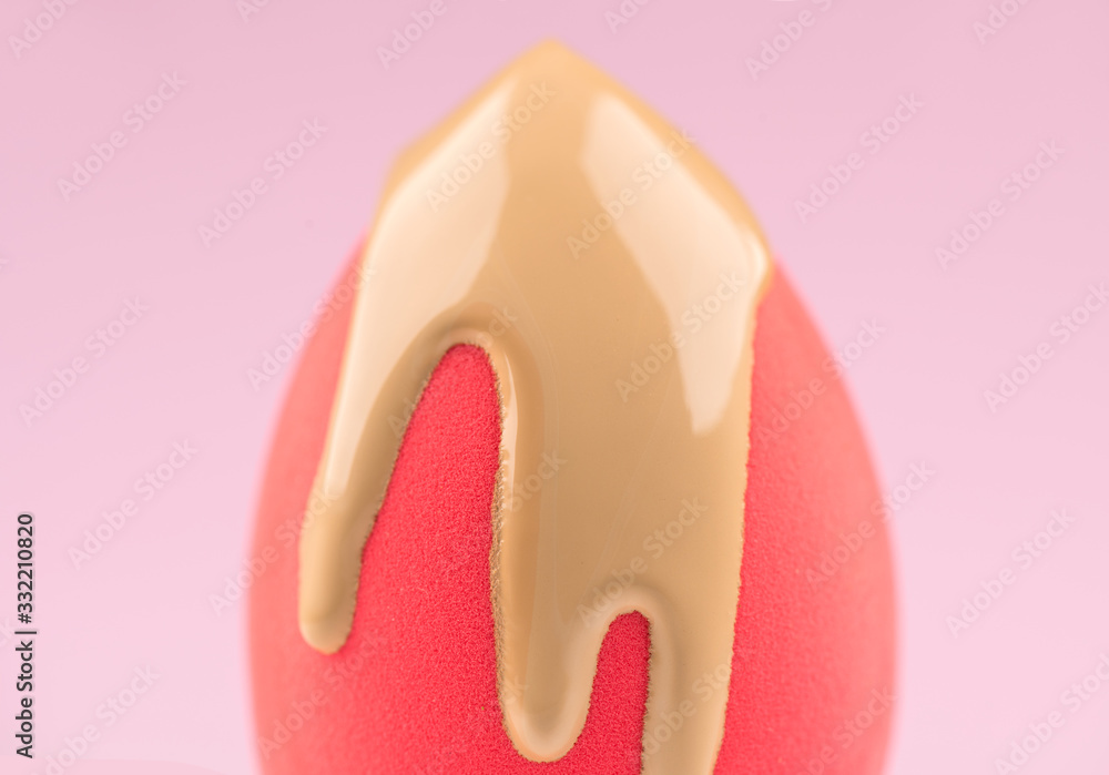 Makeup liquid foundation pouring on pink make-up blender sponge, closeup. Applying Foundation beauty