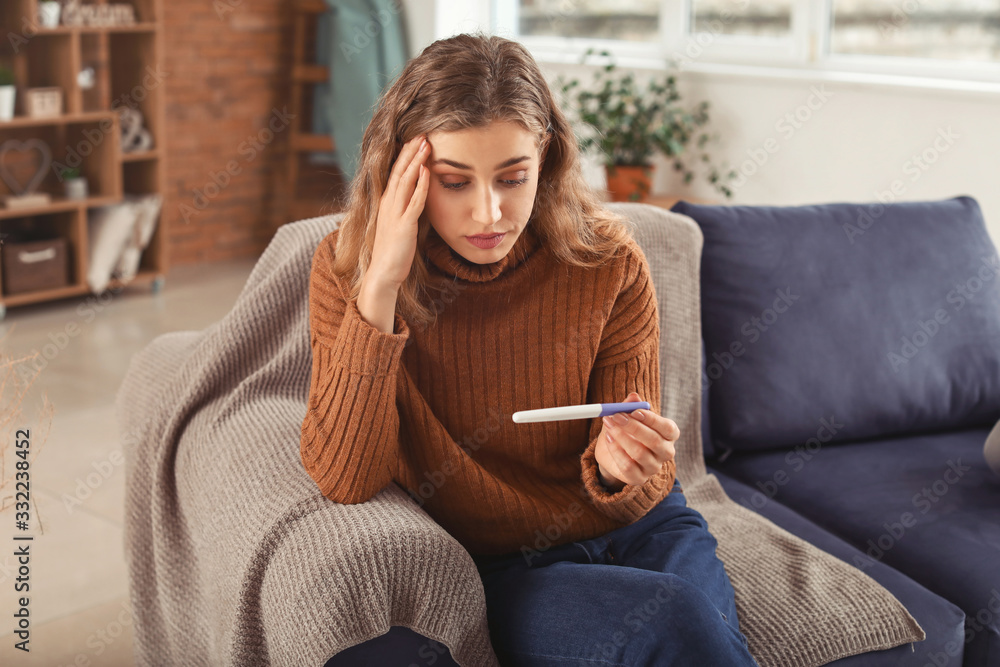 Sad young woman with pregnancy test at home