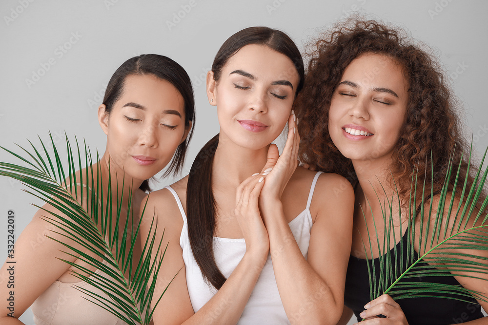 Beautiful young women with healthy skin and tropical leaves on light background