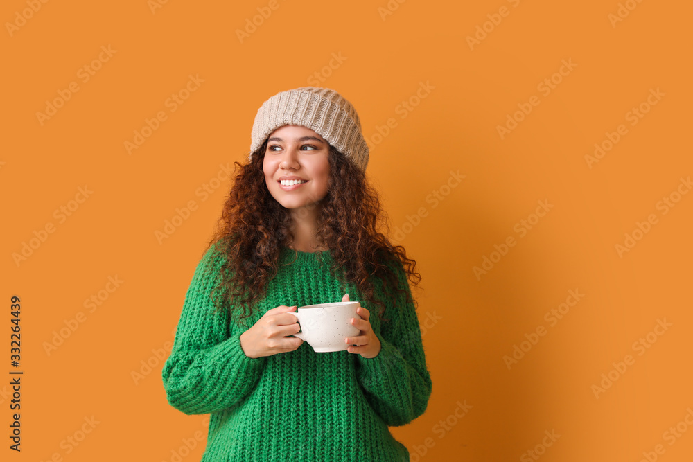 Young woman in warm sweater and with cup of hot tea on color background