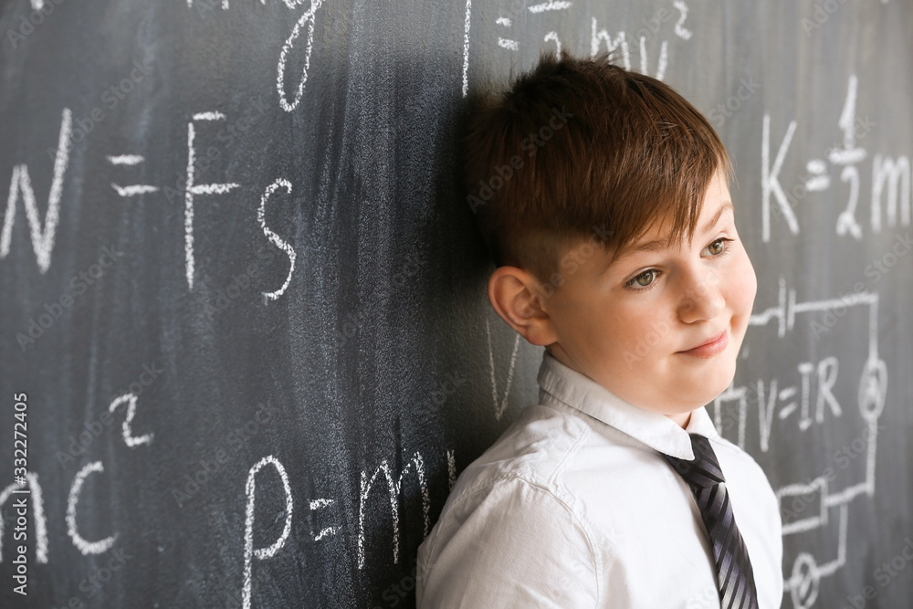 Cute little boy near blackboard at physics lesson in classroom