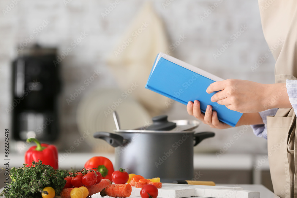 Woman with cook book preparing food in kitchen