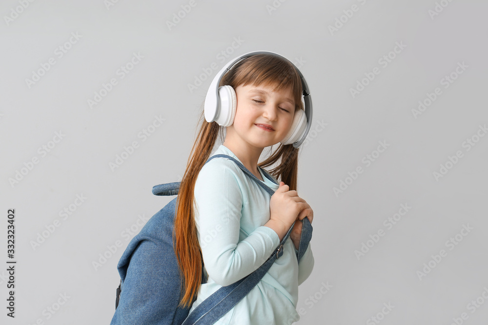 Cute little schoolgirl with headphones on grey background