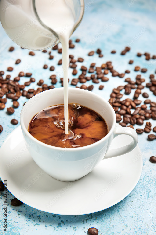 Pouring of milk in cup of hot coffee on table