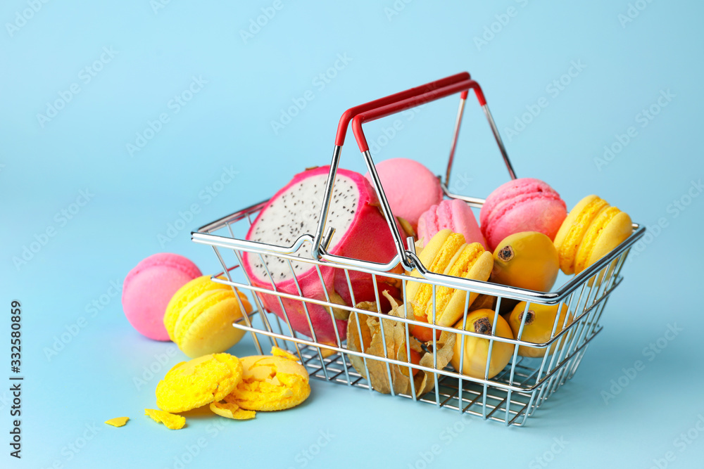 Tasty macarons with fruits in shopping basket on color background