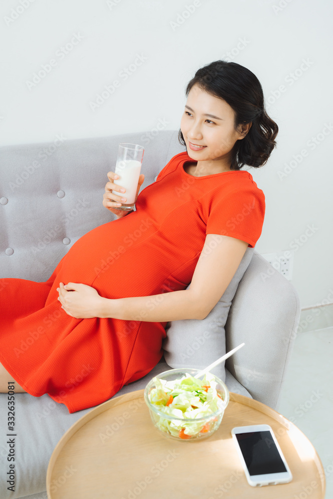 Young pregnant woman having breakfast with salad and milk.