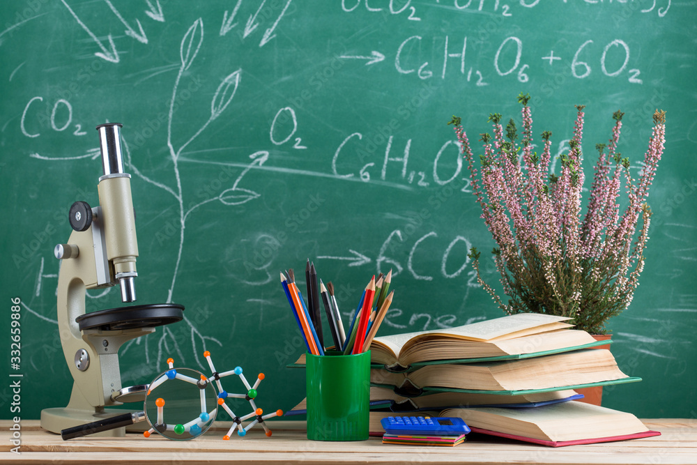 Education and sciences concept - books, molecule model and microscope on the desk in the auditorium,