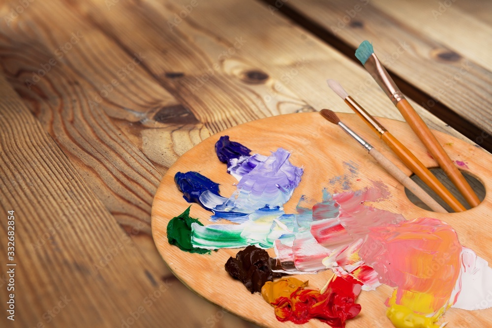 Wooden art palette with blobs of paint and  brushes on desk