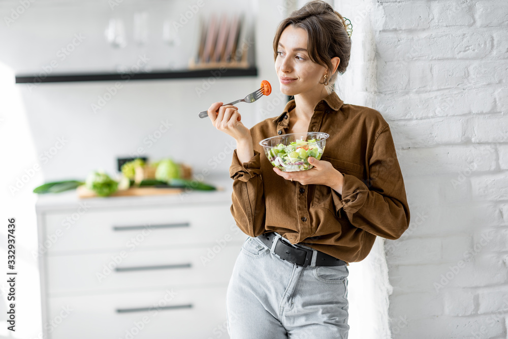 Portrait of a young and cheerful woman eating healthy salad on the kitchen at home. Healthy eating, 