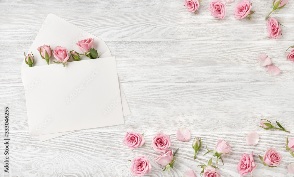 Blank envelope with rose flowers on wooden background. Top view of pink roses and rosebuds. Happy Mo