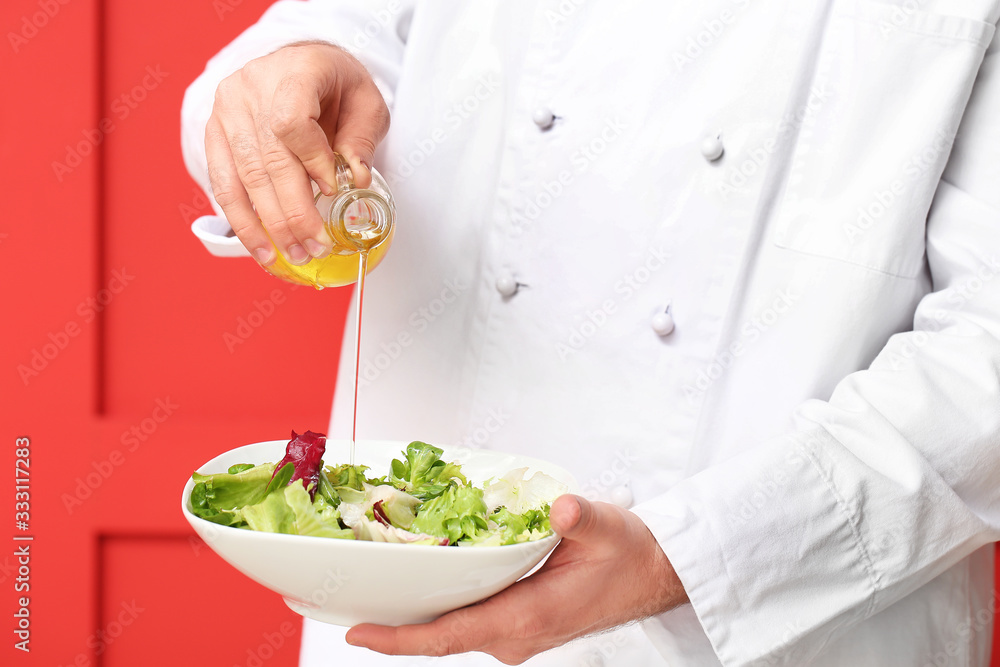 Handsome male chef dressing salad on color background, closeup