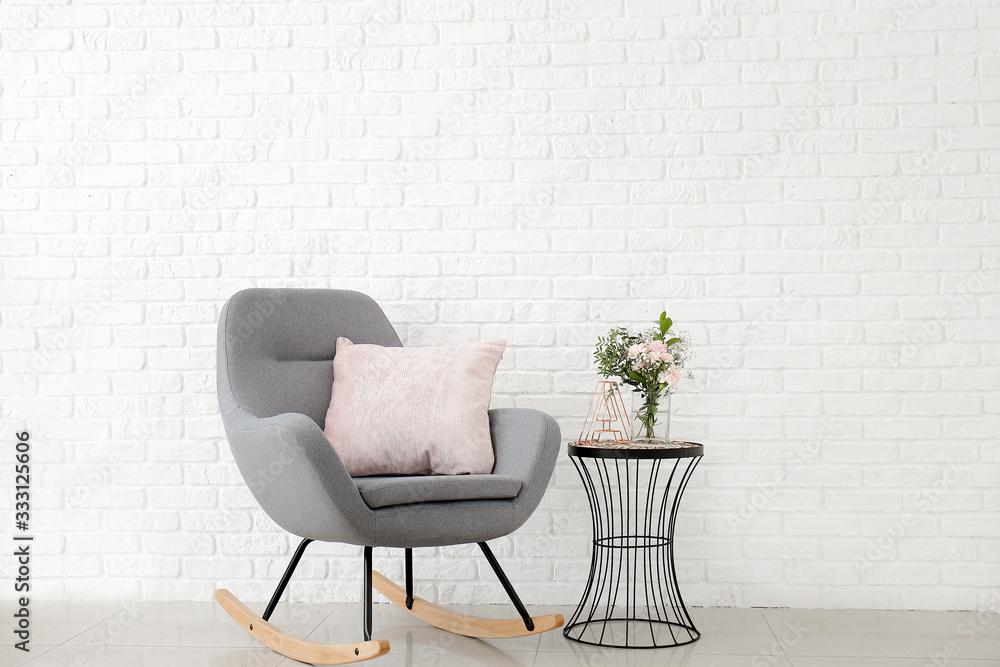 Interior of modern room with comfortable armchair and table with spring flowers near brick wall