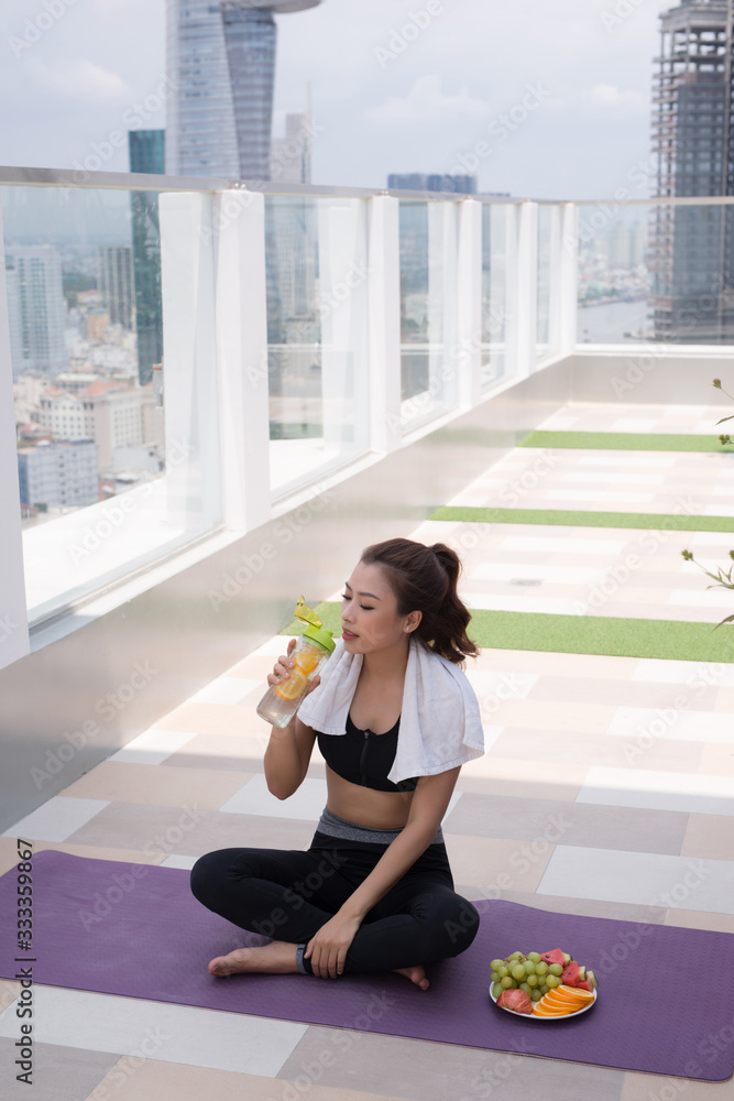 一位美丽的年轻女子坐在瑜伽垫上，在一个建筑屋顶上剧烈锻炼后休息