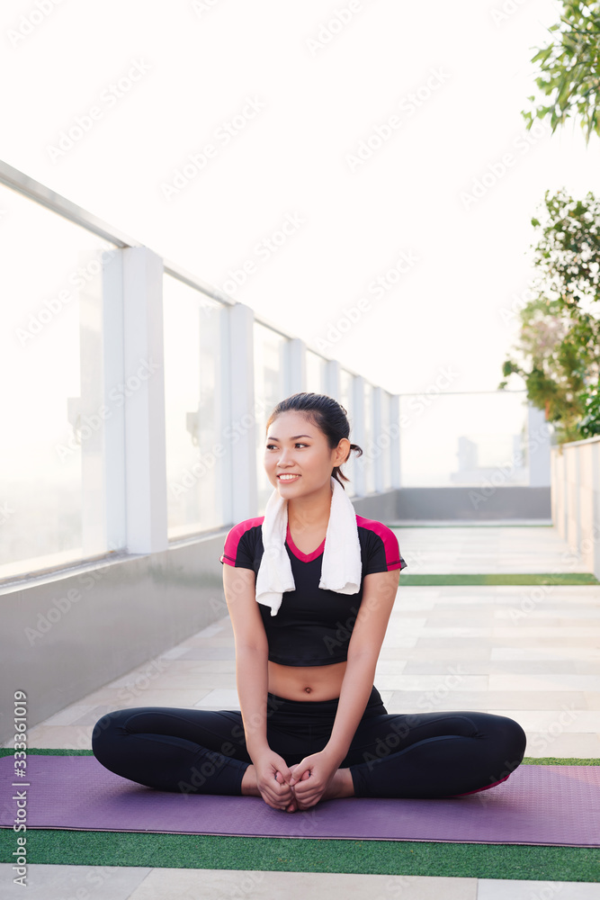 Young beautiful Asian woman sitting on yoga mat and smiling in morning. Sport and healthy lifestyle.