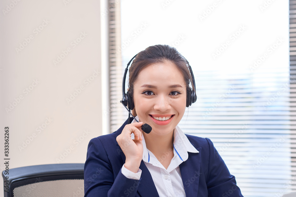 Portrait of happy smiling female customer support phone operator at workplace. Asian