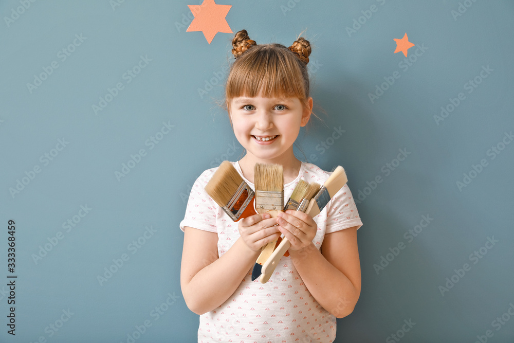 Little girl with paint brushes near color wall