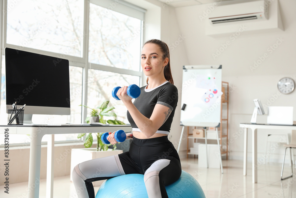 Young woman doing exercises with fitness ball in office