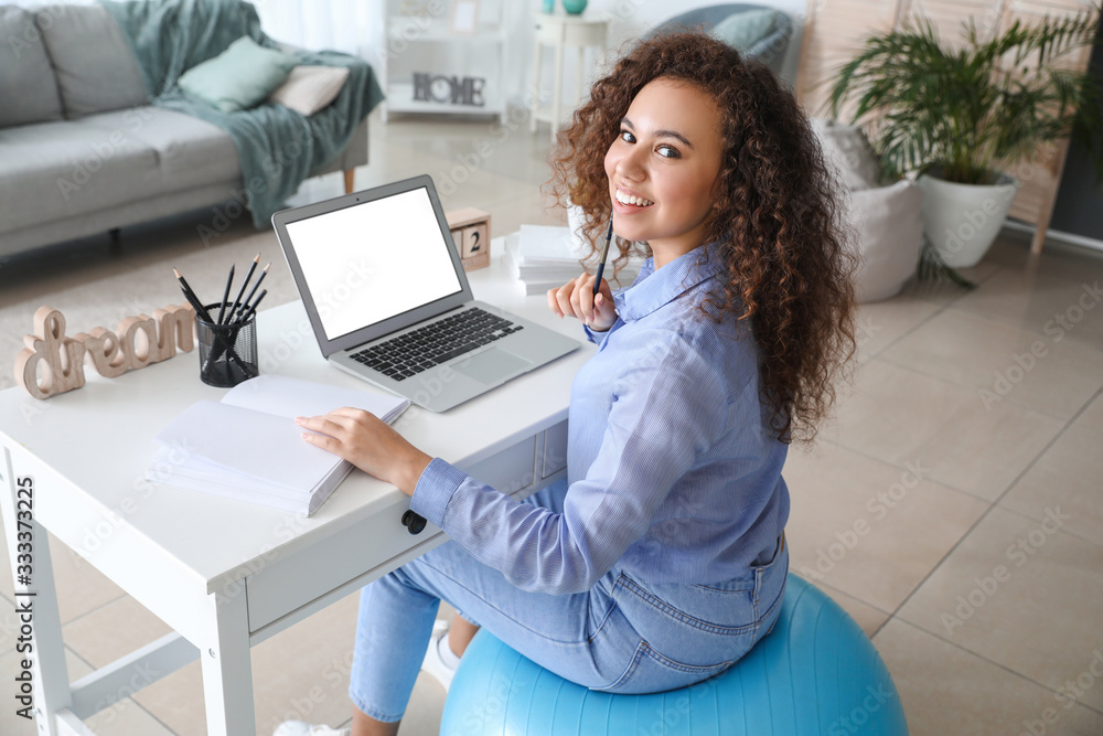 Woman sitting on fitness ball while working at home