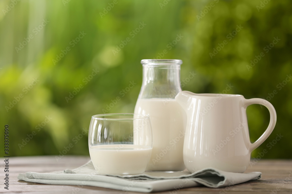 Glass, jug and bottle of fresh milk on table outdoors