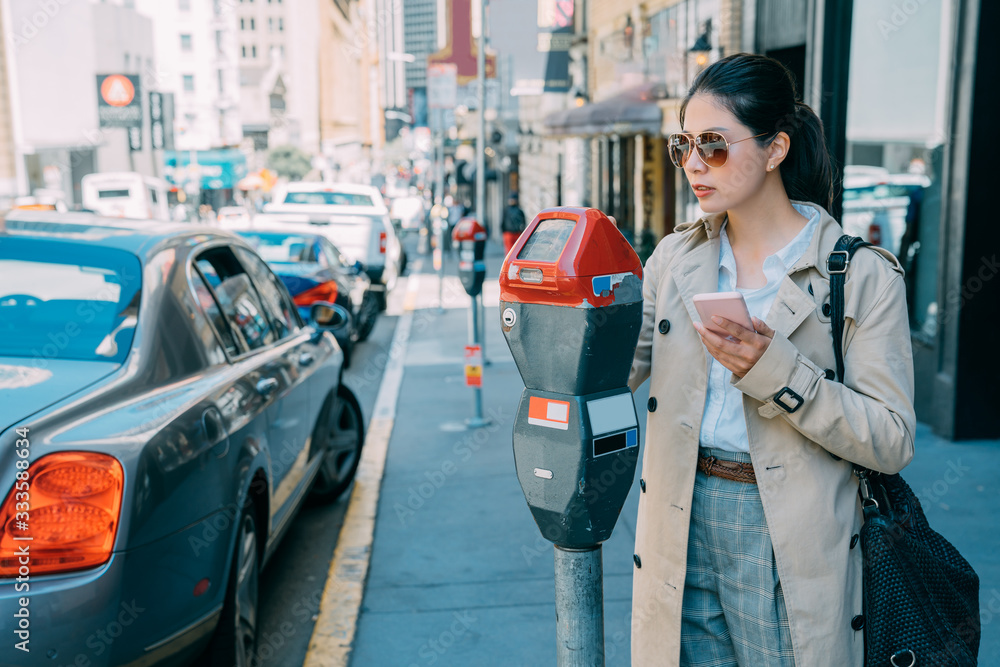 Young charming asian Japanese woman paying for car parking at machine with mobile phone online app. 