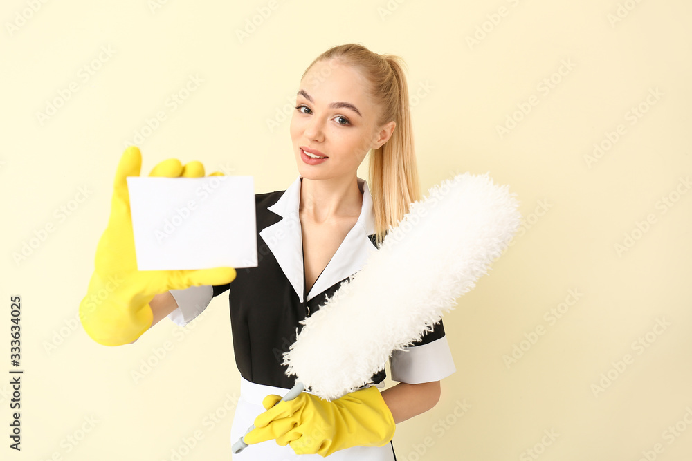 Beautiful young chambermaid with business card on light background