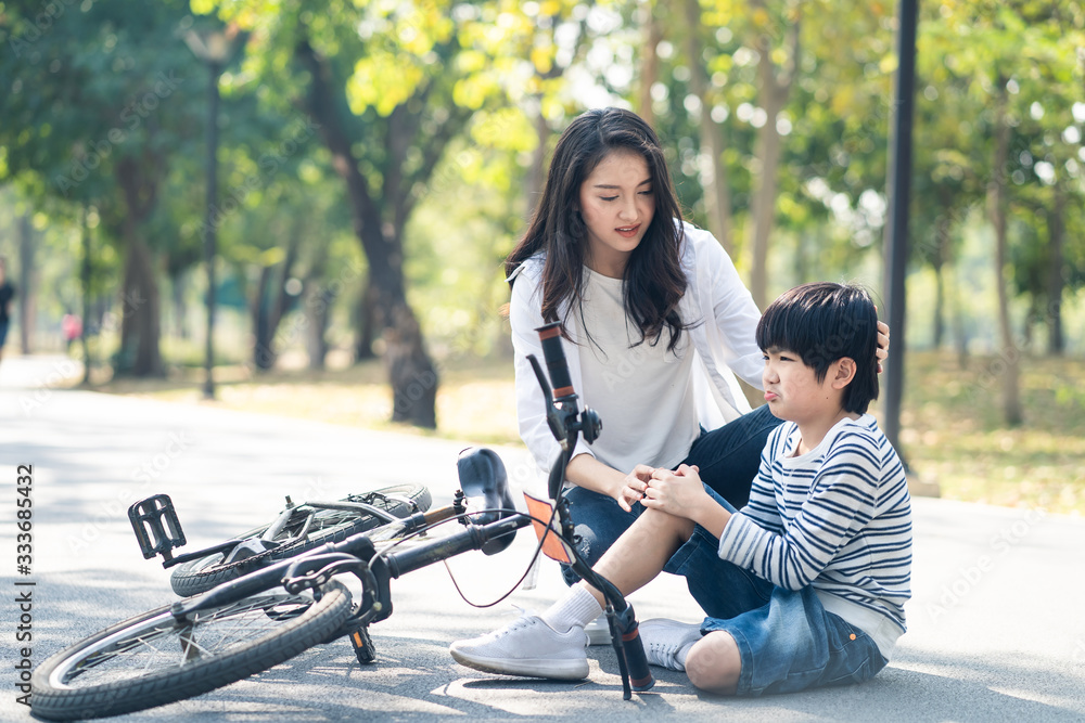 Asian young mother encourage son to ride bicycle in park. Mother sit beside kit, hold son hand and h