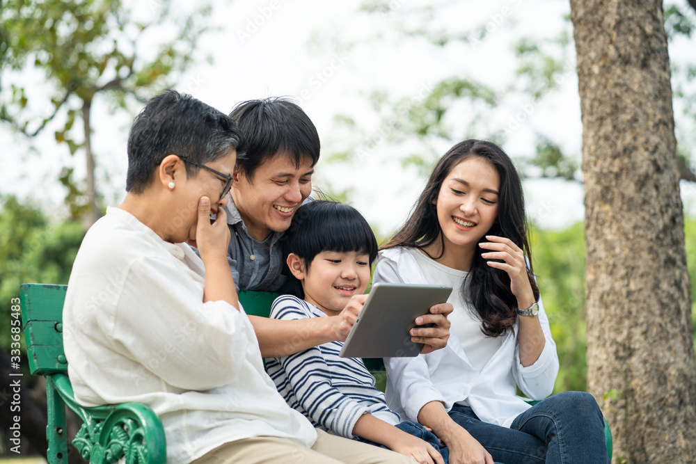 Asian happy family play in park, read electronic book from tablet together. Boy sit in on bench betw