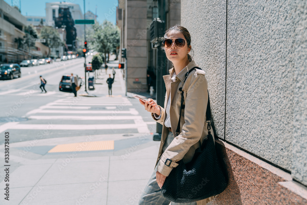 Young attractive woman in sunglasses stands outside on wall background. beautiful asian lady looking