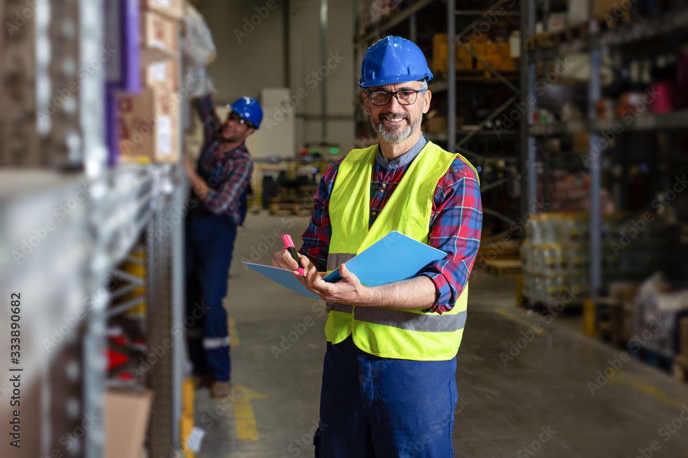 Warehouse manager writing on clipboard in a large warehouse